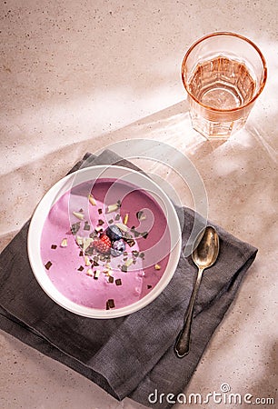 A summer dinner made of a big bowl of berries yoghourt with some chocolate and nuts as topping and a glass of water Stock Photo