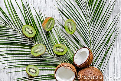 Summer exotic fruits. Kiwi, coconut and palm branch on wooden background top view Stock Photo