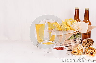 Summer fast food - different crunchy snacks, two lager beer in glass and brown bottles on soft white wood board. Stock Photo