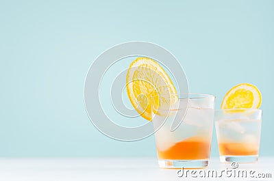 Summer fresh cold cocktail with oranges, ice, piece fruit on soft light pastel green background and white wood table. Stock Photo