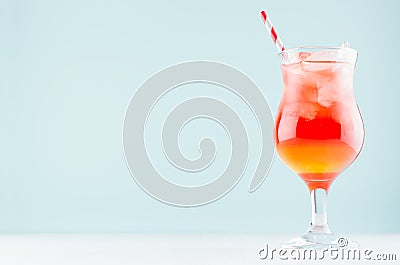 Summer fresh fruit layered red, yellow sunrise cocktail with straw, ice cubes in wineglass on pastel green background. Stock Photo