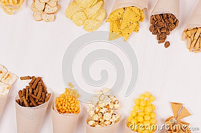 Summer fun fast food - different crunchy snacks in craft paper cornet as decoration border on soft white wood board. Stock Photo