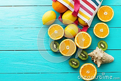 Summer fun time and fruits on blue wooden background. Orange, lemon, kiwi fruit in bag and shell Stock Photo