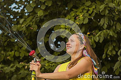 Summer garden, watering - beautiful girl watering roses with garden hose in the garden Stock Photo