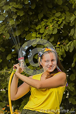 Summer garden, watering - beautiful girl watering roses with garden hose in the garden Stock Photo