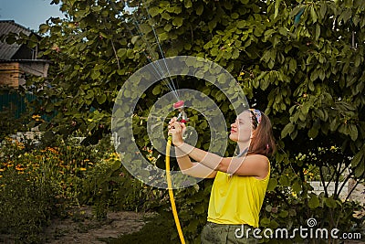 Summer garden, watering - beautiful girl watering roses with garden hose in the garden Stock Photo