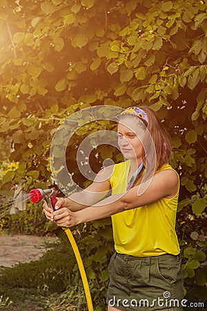 Summer garden, watering - beautiful girl watering roses with garden hose in the garden Stock Photo