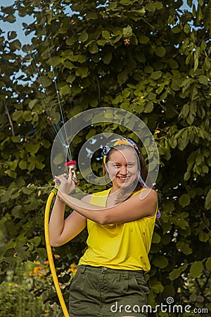 Summer garden, watering - beautiful girl watering roses with garden hose in the garden Stock Photo