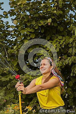 Summer garden, watering - beautiful girl watering roses with garden hose in the garden Stock Photo