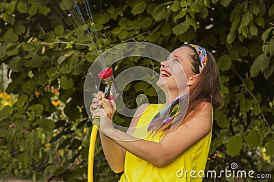 Summer garden, watering - beautiful girl watering roses with garden hose in the garden Stock Photo