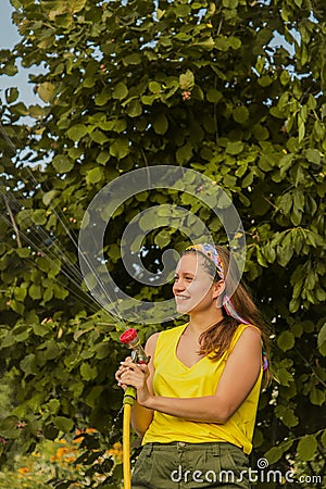 Summer garden, watering - beautiful girl watering roses with garden hose in the garden Stock Photo