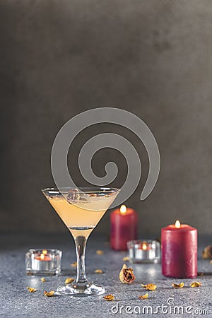 Summer grapefruit martini cocktail with dried roses flowers and petals, surrounded candles on dark gray table surface Stock Photo