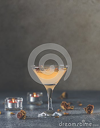 Summer grapefruit martini cocktail with dried roses flowers and petals, surrounded candles on dark gray table surface Stock Photo