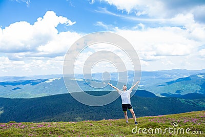 Summer hiking in the mountains. Young tourist man in a cap with hands up on the top of the mountains admires the nature Stock Photo