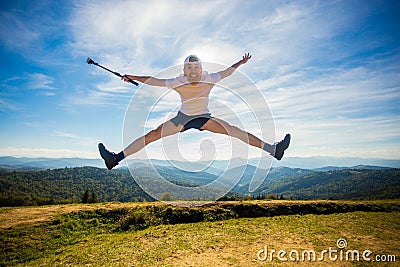 Summer hiking in mountains. Young tourist man in cap with hands up on top of mountains admires nature Stock Photo