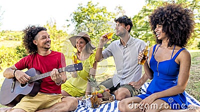 Summer holidays outdoor picnic. multiracial group of friends having food and drinking beers laying on a blanket in a park garden. Stock Photo