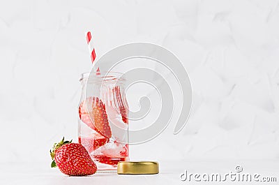 Summer homemade drink - infused strawberry water with sliced berry, ice cubes, soda, cap, straw in soft light white interior. Stock Photo