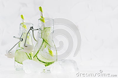 Summer homemade drinks - infused green cucumber water with slices, soda, straw, ice cubes in yoke bottles in soft light white . Stock Photo