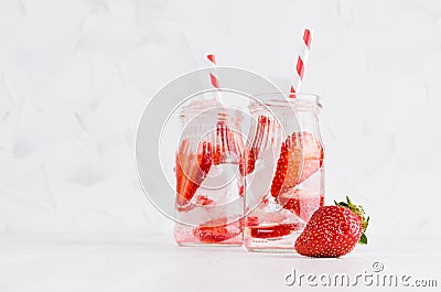 Summer homemade drinks - infused strawberry water with sliced berry, ice cubes, soda, straw in soft light white interior. Stock Photo