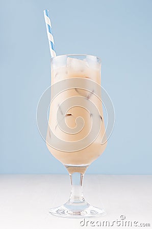 Summer ice coffee cocktail with ice cubes and striped straw on soft light blue wall and white wooden table, vertical. Stock Photo