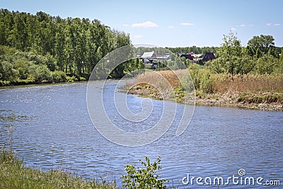 Summer landscape - a calm flat river among fields and birch groves under a blue sky. Village houses on the other side. Stock Photo