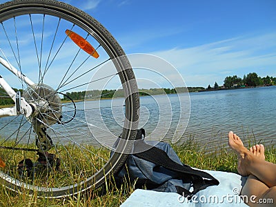 Summer landscape bike whell and barefoot legs girl resting on a lake blue sky background Stock Photo