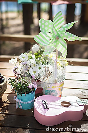 Summer outdoor birthday party decoration on a wooden table. Green pinwheel, flowers and pink ukulele Stock Photo