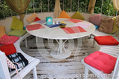 Summer pavilion with white round table and multicolored pillows. Stock Photo