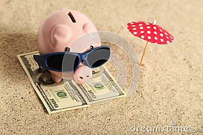 Summer piggy bank standing on towel from greenback hundred dollars with sunglasses on the beach and red parasol Stock Photo