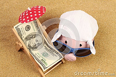 Summer piggy bank with sunglasses and hankie next to beach chair with towel from greenback hundred dollars and red parasol on sand Stock Photo