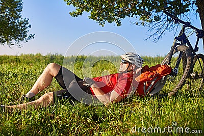 Summer portrait of handsome young man lying on green meadow near bike and backpack. Stock Photo