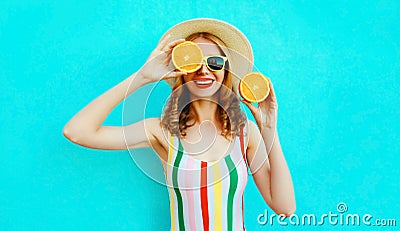 Summer portrait smiling woman holding in her hands two slices of orange fruit hiding her eye in straw hat on colorful blue Stock Photo