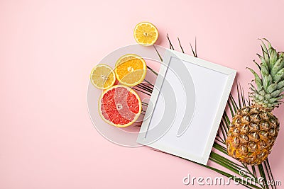 Summer rest concept. Top view photo of white photo frame and ripe tropical fruits cut lemon orange grapefruit pineapple and palm Stock Photo