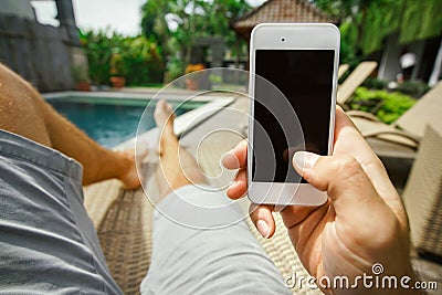 Summer rest. Relax in the hotel with a phone in hand. A man lying on a lounger by the pool and enjoying your smartphone. Stock Photo