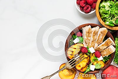 Summer salad with grilled chicken and peach, feta cheese and raspberries in a bowl with fork. healthy food. top view Stock Photo