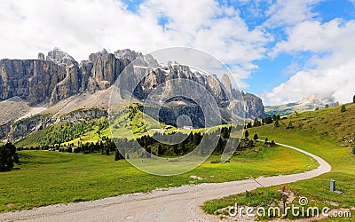 Summer scenery of majestic Sella Mountains & hiking trails winding in the green grassy valley on a cloudy sunny day Stock Photo
