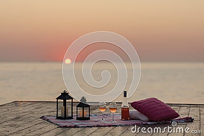 Summer sea sunset. Romantic picnic on the beach. Bottle of wine, glasses, candles, plaid and pillows. Stock Photo