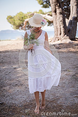 Summer Serenity: Barefoot Girl in White Dress with Straw Hat and Flowers by the Sea Stock Photo