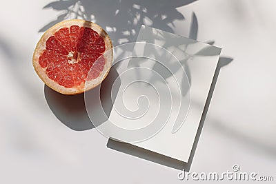 Summer stationery still life scene. Closeup of cut grapefruit fruit on white table background in sunlight. Blank paper Stock Photo