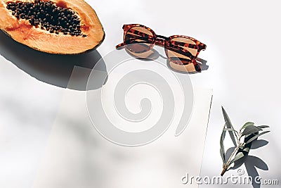Summer stationery still life scene. Closeup of cut papaya fruit, olive branch and sunglasses in sunlight. White table Stock Photo