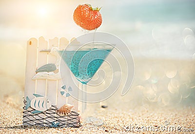 Summer still life on the beach. Glass with a drink and nautical scenery against the backdrop of the sea and the beach. Stock Photo