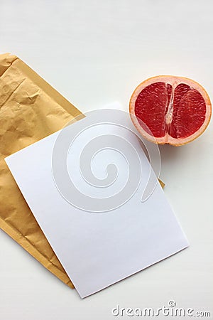 Summer still life with half of grapefruit, blank paper card and golden envelope on white background. Invitation mockup. Stock Photo