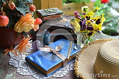 Summer still life with old decorated book, crystal stines and beautiful flowers in pots outside in the garden. Vintage Stock Photo