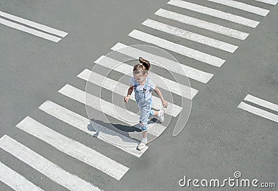 In the summer on the street at the pedestrian crossing kid girl in fashion clothes cross the road. From top view. Shadow at zebra Stock Photo