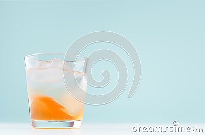 Summer striped oranges lemonade with ice cube, liquor in misted glass on elegant pastel green wall, white wood table. Stock Photo