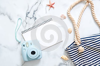 Summer travel composition on a marble background. Women`s desk with instant photo camera, striped beach bag, seashells and blank n Stock Photo