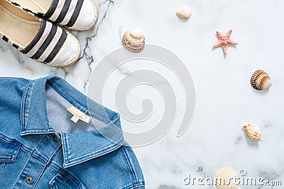 Summer vacation composition. Fashionable jeans jacket, striped summer sandals, seashells, sea star on marble background. Women`s d Stock Photo