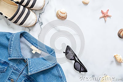 Summer vacation composition. Fashionable jeans jacket, sunglasses, striped sandals, seashells, sea star on marble background. Wome Stock Photo