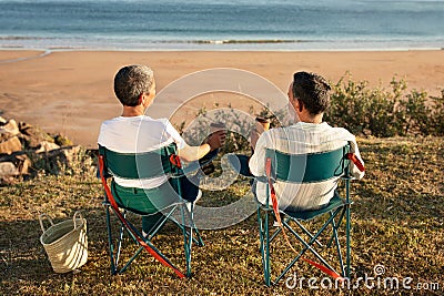 Older couple sitting together facing ocean enjoying coffee at seaside Stock Photo