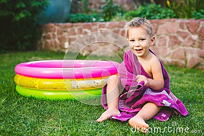 Summer vacation theme. A small 3 year old Caucasian boy playing in the backyard of a house on the grass near a round inflatable co Stock Photo